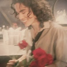 a man with long curly hair is holding roses in his hand and smiling at the camera