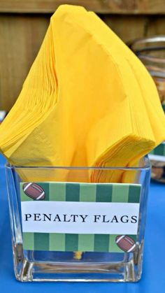 a yellow napkin sits in a clear cup on top of a blue table cloth covered table