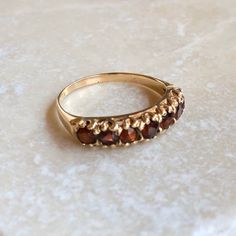 A Vintage 9 carat gold Garnet band. This beautiful piece holds all seven garnets neatly in line, what a gorgeous collection of glowing red stones. The setting holds each stone in it’s clutches while displaying all the sparkle from them. This piece is special and a total stunner!CONDITION: Wear consistent with age and use. Please see photos for more detail.APPROX. SETTING (ACROSS): 22mmAPPROX. BAND WIDTH: 1.5mmRING SIZE: UK: N | US: 6 1/2WEIGHT: 1.9 gramsTHANK YOU FOR LOOKING :) Classic Stone Rings For Formal Occasions, Classic Rings With Stones For Formal Occasions, Classic Formal Rings With Stones, Gold Multi-stone Garnet Jewelry, Gold Garnet Multi-stone Jewelry, Vintage Yellow Gold Half Eternity Jewelry, Vintage Half Eternity Jewelry As A Gift, Red Stones, White Sapphire Ring