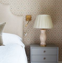 a nightstand with a lamp on top of it next to a white bed in a bedroom