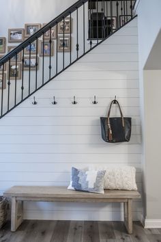 a wooden bench sitting under a stair case next to a wall with pictures on it