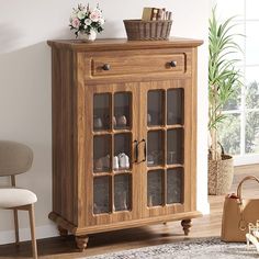 a wooden cabinet with glass doors in a living room next to a chair and potted plant