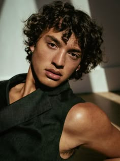 a young man with curly hair is posing for the camera, wearing a black shirt