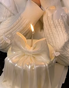 a white cake with a candle in the middle on a table next to gloves and sweaters