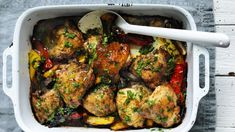 a white casserole dish filled with chicken, vegetables and herbs on a wooden table