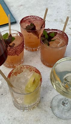 four glasses filled with different types of drinks on top of a white countertop next to each other