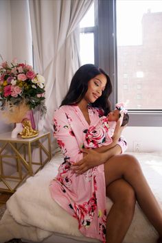 a woman sitting on a bed in a pink robe holding a cell phone and smiling at the camera