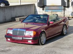 a red convertible car parked in a parking lot next to a wall and concrete structure