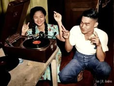 a man and woman sitting next to each other in front of a record player