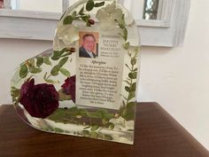 a heart shaped glass frame with flowers and leaves on the inside is shown in front of a window