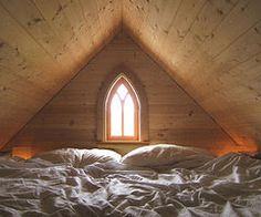 a bed with white sheets and a window in the middle of it on top of a wooden wall