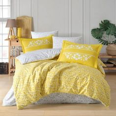 a bed with yellow and white comforters in a room next to a potted plant