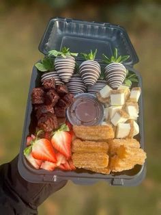 a person holding up a tray with strawberries, chocolate covered strawberries and other foods