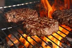 hamburgers cooking on an open grill with flames in the backgroung, closeup