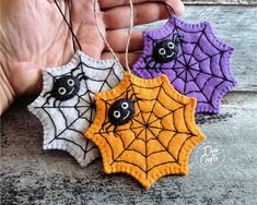 three handmade halloween decorations hanging from string on wooden surface with spider web and bats