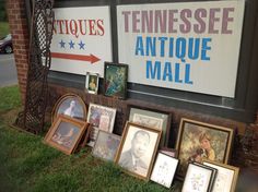 many framed pictures are on display in front of an antique mall sign and other memorabilia