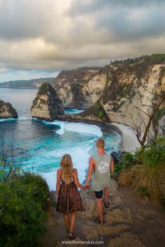 two people are walking up the stairs towards the water's edge with cliffs in the background