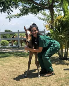 a woman in scrubs is petting a small horse on the grass near some trees