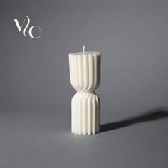 a tall white candle sitting on top of a gray table next to a black and white logo