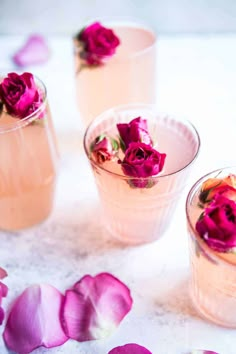 three glasses filled with pink flowers on top of a white table next to rose petals