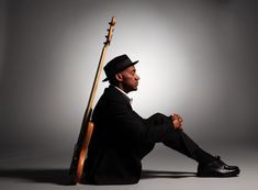 a man sitting on the ground with a guitar in his lap and wearing a hat