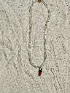 a necklace with a red and green pepper hanging from it's side on a white sheet