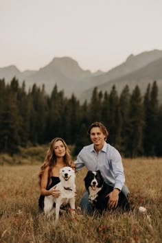 a man and woman are sitting in the grass with their dog