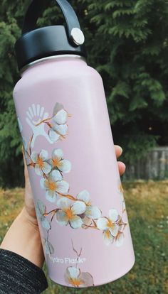 a hand holding a pink water bottle with white flowers on it