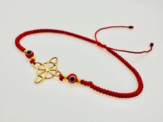 Es una pulsera adornada con chaquiras rojas tiene un ojito cada lado y cómo Simbolo principal un nudo de bruja