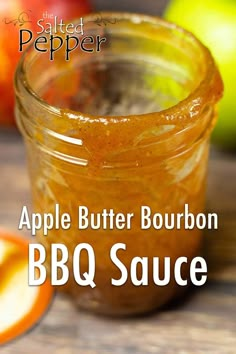 an apple butter bourbon bbq sauce in a glass jar next to sliced apples on a wooden table