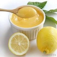 a spoon with some lemon on it next to a bowl of liquid and two lemons