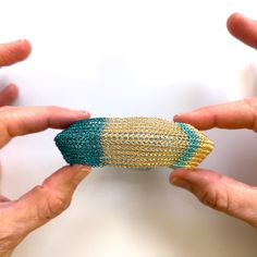 two hands holding an object in the shape of a ball with green and yellow stripes