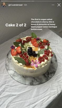 a cake with berries and other fruits on it sitting on top of a white table cloth