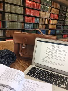 an open laptop computer sitting on top of a wooden table next to a book case