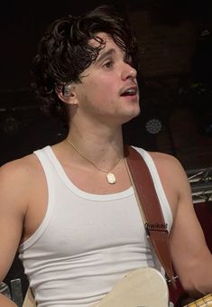 a young man holding a guitar in his right hand and wearing a white tank top