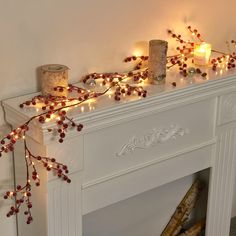 a white fireplace with candles and red berries on the mantle next to it is decorated with christmas lights