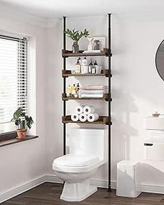 a white toilet sitting next to a window in a bathroom under a mirror with shelves on it