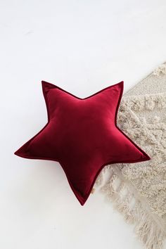 a red star shaped pillow sitting on top of a white carpet next to a throw blanket