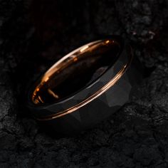 a black and gold ring sitting on top of a rocky surface with the light shining through it