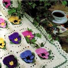 crocheted pansies on a table next to a cup of coffee and flowers