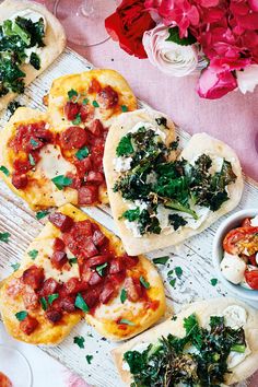 several flat bread pizzas with toppings on a white tray next to red flowers