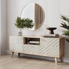 a white and wood sideboard with a round mirror on it's wall next to a potted plant