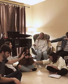 a group of people sitting on the floor in front of a black piano with their hands up