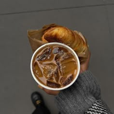 a person holding a cup of iced coffee and croissant