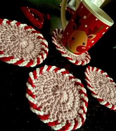 three crocheted coasters on a table next to a coffee cup and mug