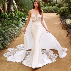 a woman in a white dress standing on a dirt path with palm trees behind her