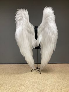 two white wings on a black stand in front of a gray wall and carpeted floor