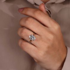 a woman's hand with a diamond ring on her left hand, wearing a beige shirt