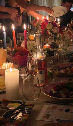 a group of people standing around a table with food and candles in the middle of it