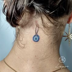 the back of a woman's neck has a blue evil eye tattoo on it